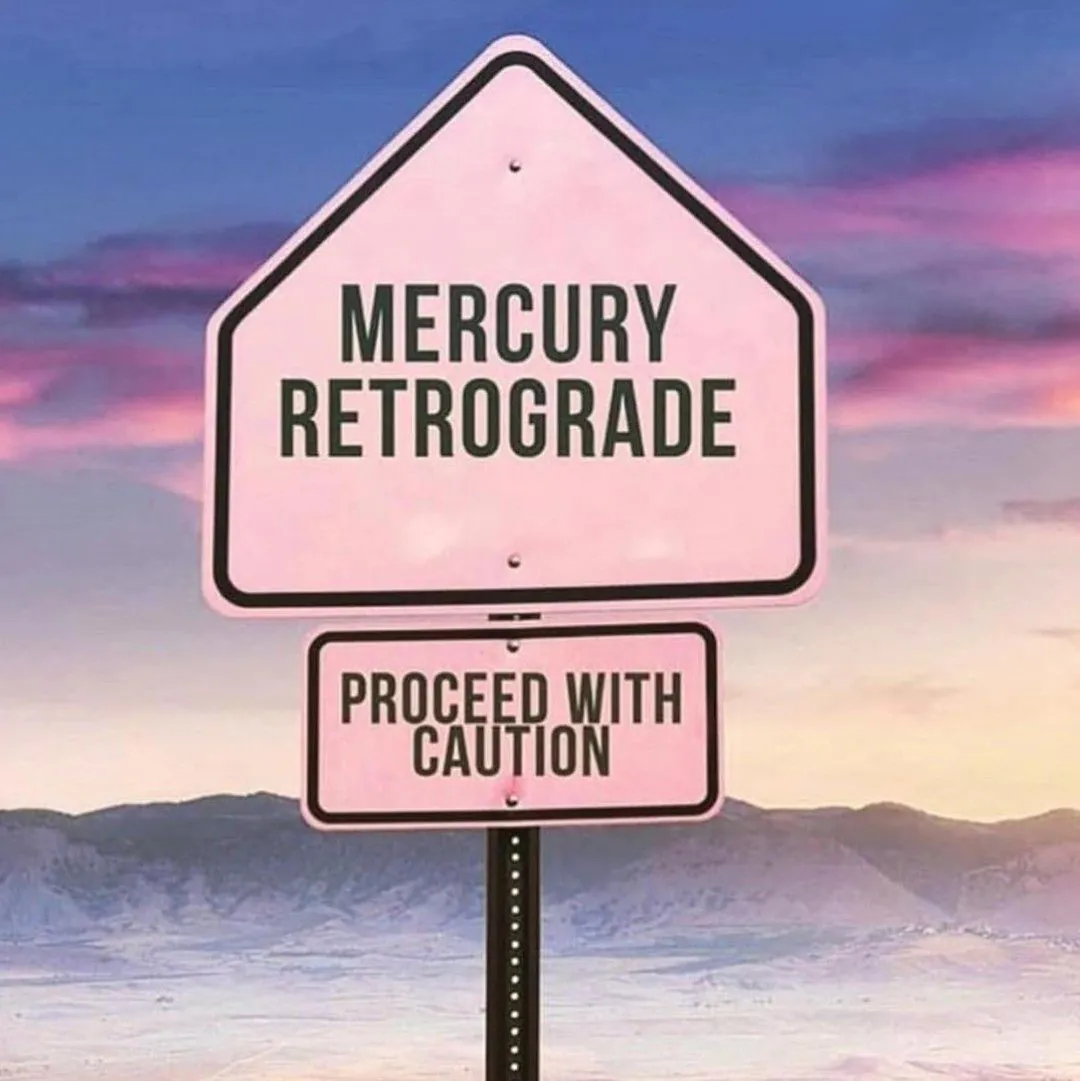 Różowy znak drogowy na tle pastelowego nieba z napisem Mercury Retrograde proceed with caution